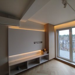 Bauel Tomasz Iskrzak - Nowoczesny salon z klimatyzacją, oświetleniem LED i zabudową meblową z drewna. Widok na balkon przez duże okno. Parkiet w jodełkę na podłodze.