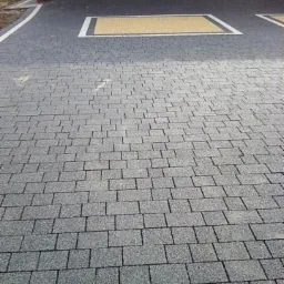 Ułożona szara kostka brukowa z prostokątną, żółtą wstawką obramowaną białym pasem, tworząca równą powierzchnię.