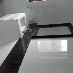 Umywalka z szafką w nowoczesnej łazience z czarnym, dekoracyjnym pasem płytek i lustrem w ozdobnej ramie.