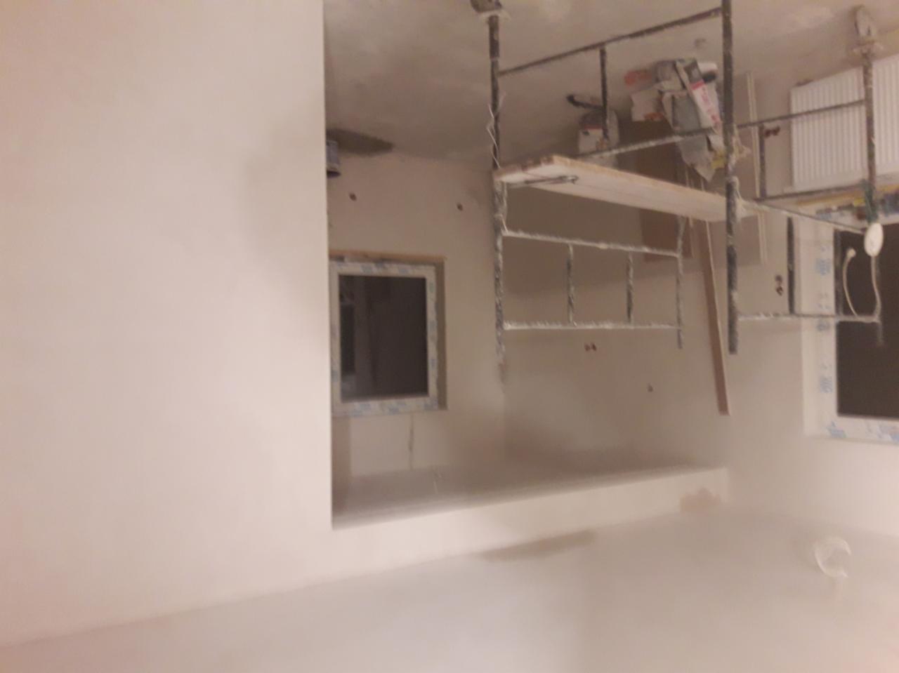 Świeżo wyszpachlowane ściany w pokoju z oknami, widoczne rusztowanie malarskie, przygotowane do dalszych prac wykończeniowych.