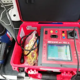 Otwarty czerwony futerał z miernikiem BENNING ST 750 A do pomiarów elektrycznych, obok opalarka Steinel HL 2010 E z widocznymi śladami użytkowania na dyszy.