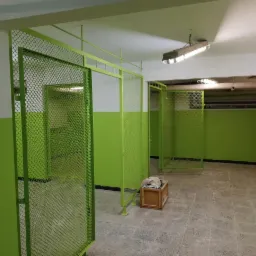 Korytarz z odnowionymi ścianami pomalowanymi na zielono i biało, z metalowymi konstrukcjami z siatki, prawdopodobnie w trakcie adaptacji pomieszczenia.