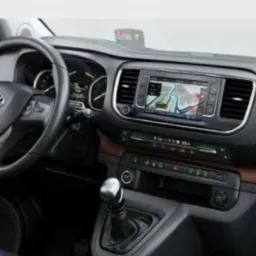 Wnętrze Toyoty Proace Verso: deska rozdzielcza z nawigacją GPS, kierownica z logo Toyota, manualna skrzynia biegów. Widok z perspektywy kierowcy.