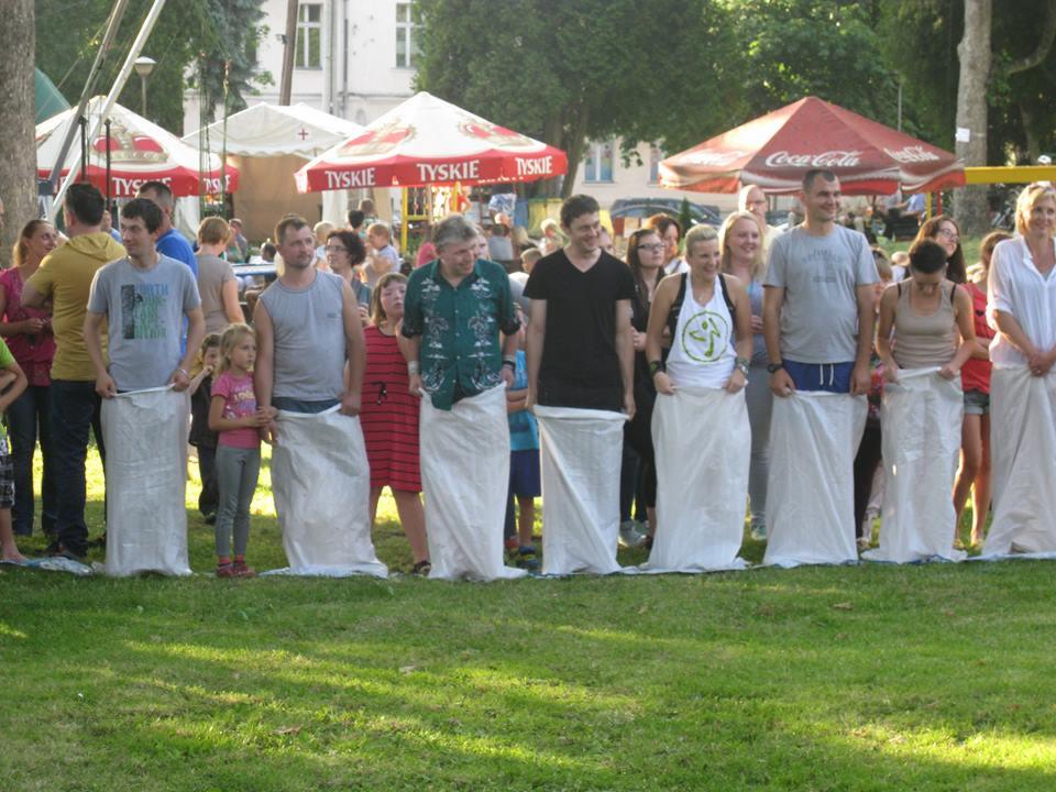 Uczestnicy w workach ustawieni na linii startu podczas konkurencji skoków w workach na imprezie plenerowej, widoczne parasole Tyskie i Coca-Cola w tle.