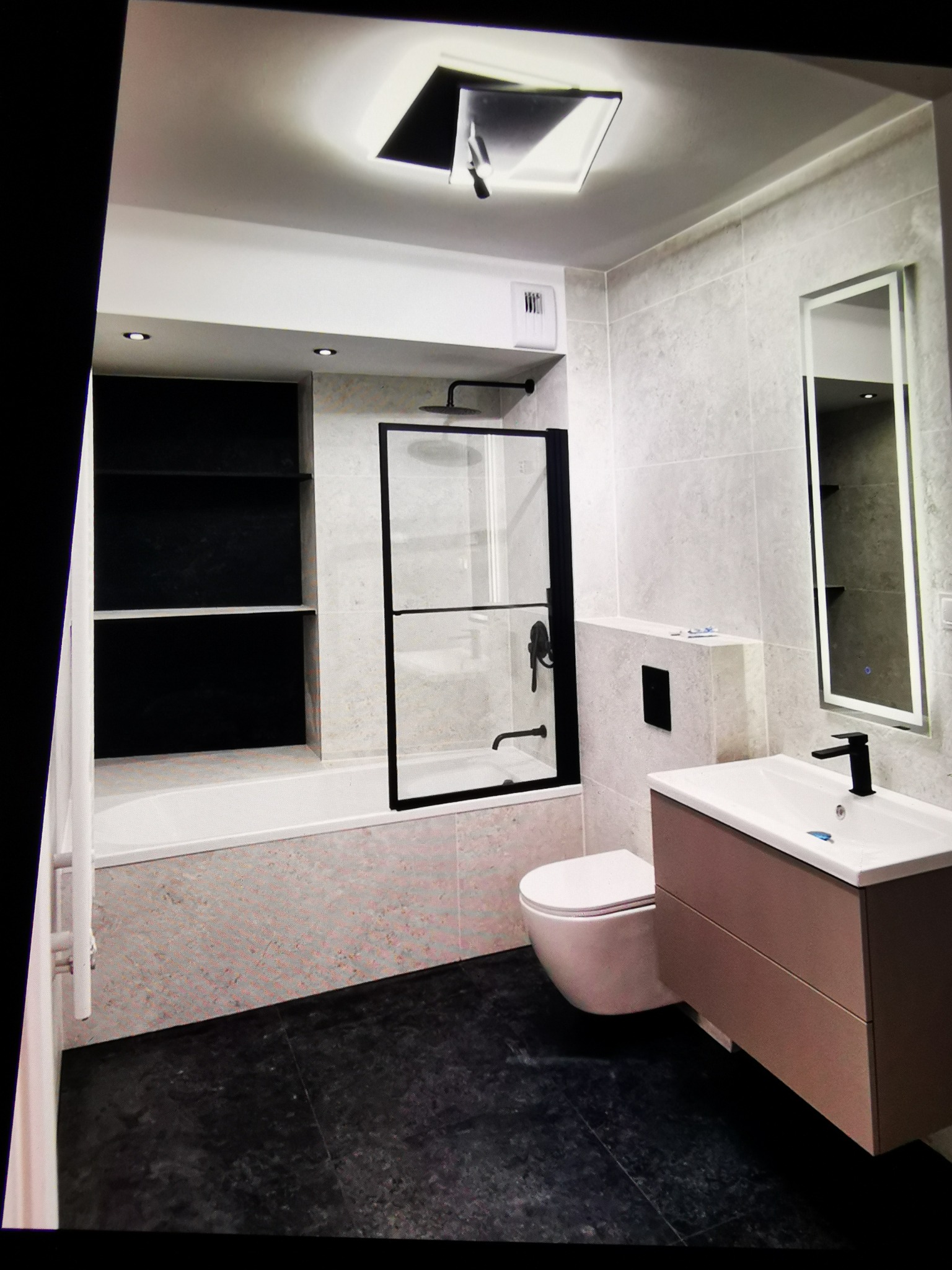 Nowoczesna łazienka z czarną armaturą i kabiną prysznicową typu walk-in, jasnymi płytkami i ciemną podłogą. Umywalka z szafką w kolorze taupe i podświetlane lustro.