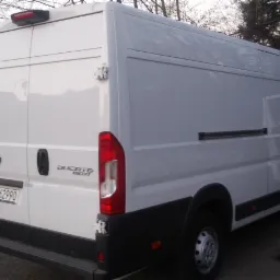 Biały furgon Ducato Maxi z otwartymi drzwiami bocznymi, zaparkowany na zewnątrz w pochmurny dzień, widok z tyłu z widoczną tablicą rejestracyjną.