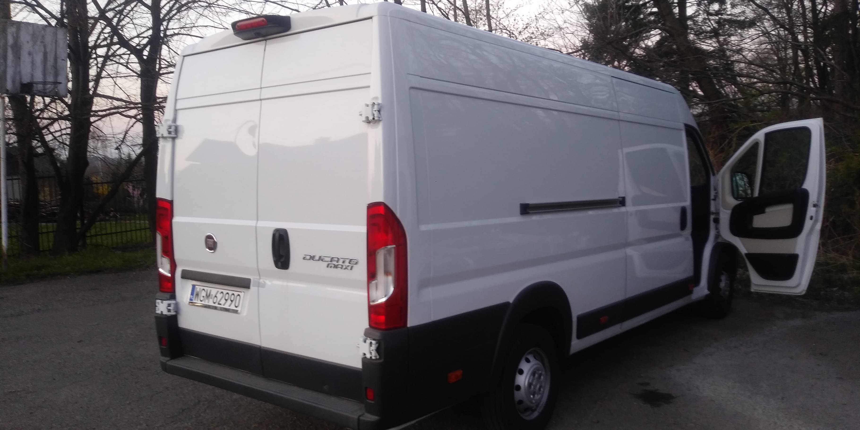 Biały furgon Ducato Maxi z otwartymi drzwiami bocznymi, zaparkowany na zewnątrz w pochmurny dzień, widok z tyłu z widoczną tablicą rejestracyjną.