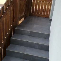 Schody wyłożone szarymi płytkami na balkonie z drewnianą balustradą i elementami konstrukcyjnymi z belek.