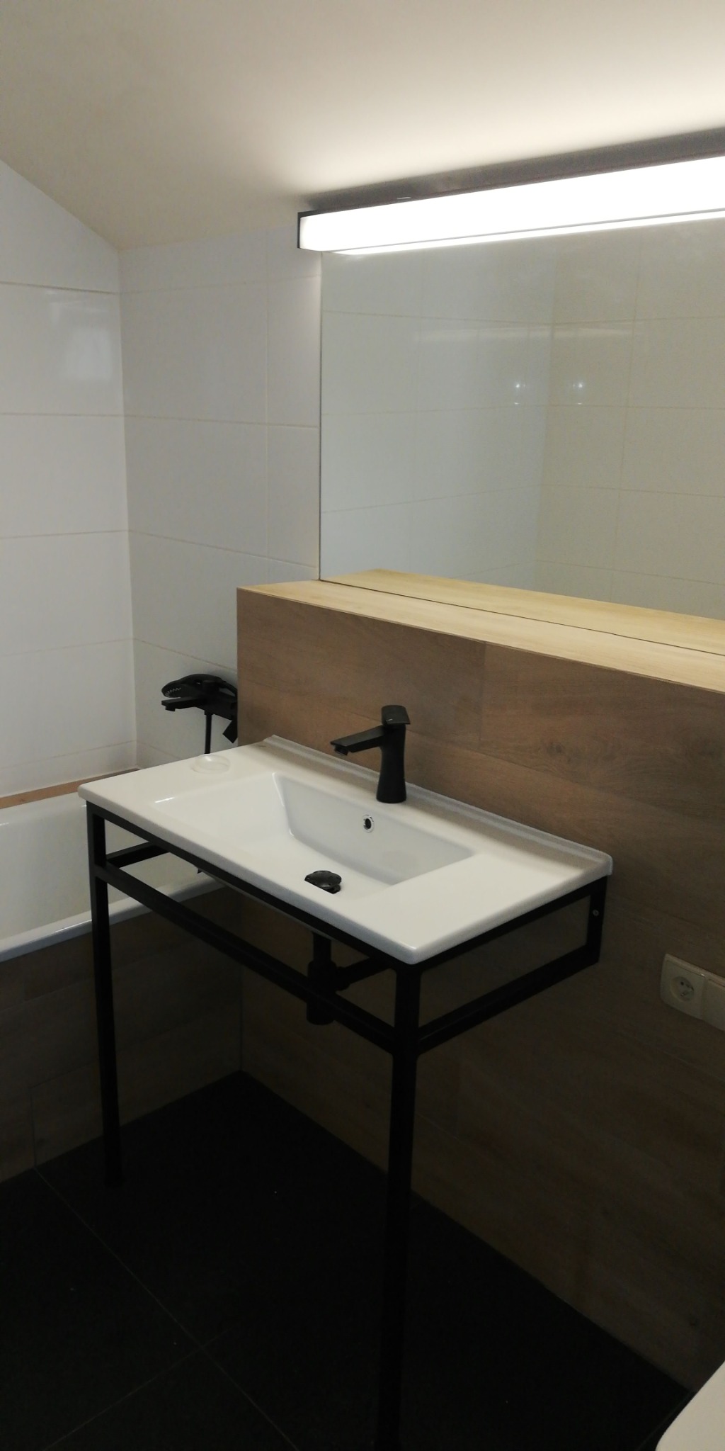 Nowoczesna umywalka nablatowa z czarną armaturą na metalowym stelażu w łazience wykończonej białymi płytkami i panelami drewnopodobnymi.