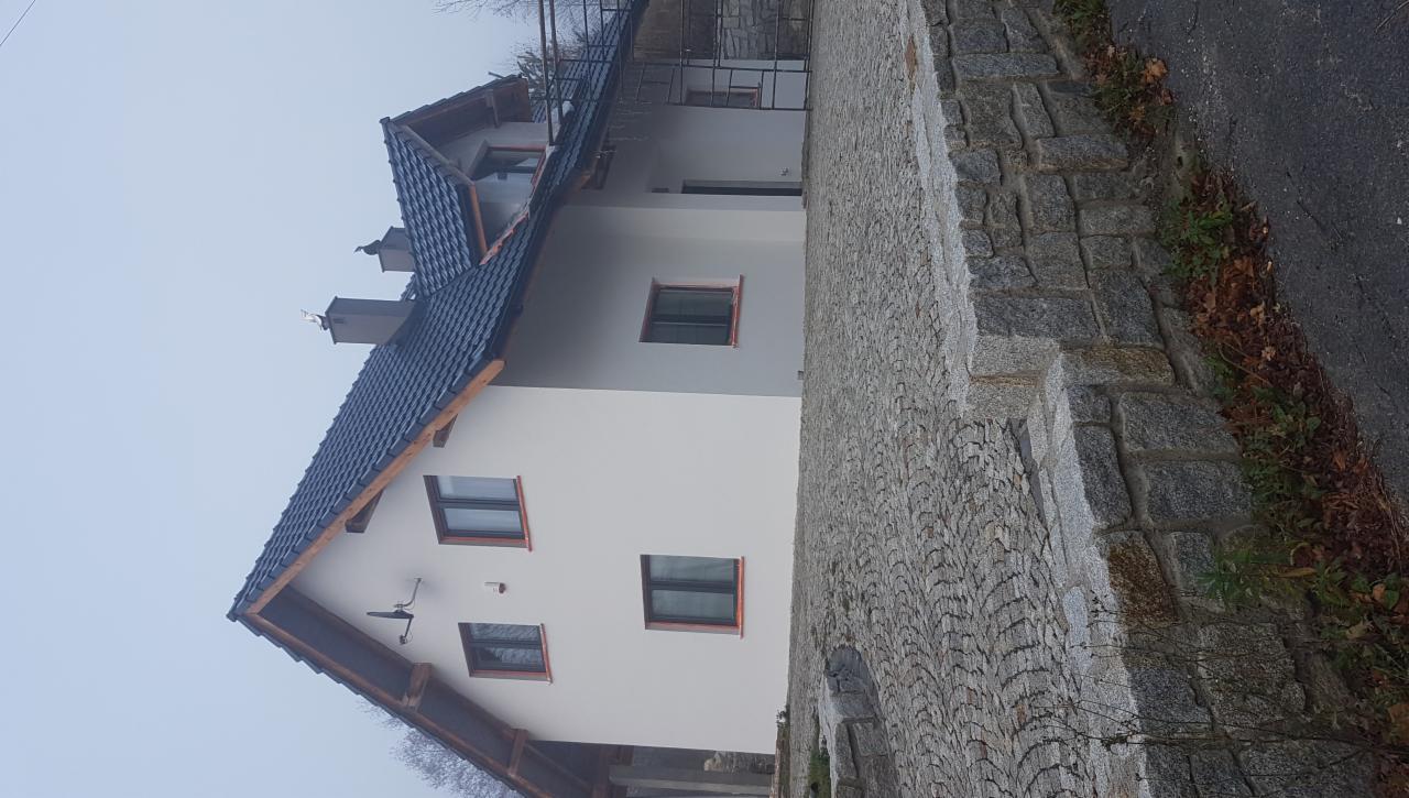 Świeżo otynkowany dom jednorodzinny z ciemną dachówką, widok z boku na elewację i kamienny chodnik.