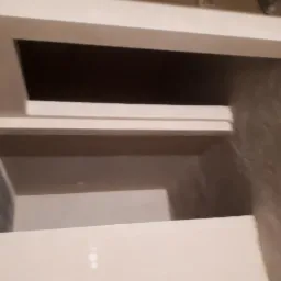 Świeżo nałożony, jasny tynk na schodach wewnętrznych, widok z dołu, surowy beton w tle.