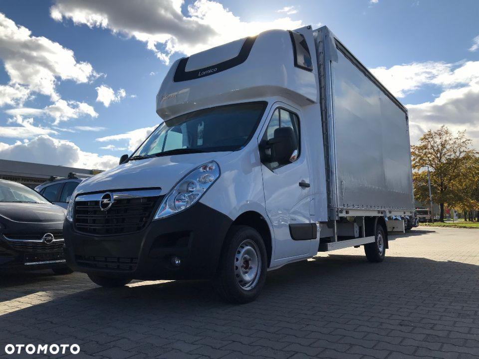 Biały samochód dostawczy marki Opel z zabudową kontenerową Lamico, zaparkowany w Krakowie na tle błękitnego nieba z chmurami i jesiennych drzew.