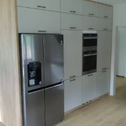 Szara kuchnia na wymiar z dużą lodówką side-by-side LG z dystrybutorem wody i kostkarką, zabudowanymi piekarnikami i szafkami górnymi z drewnianymi akcentami.