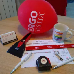 Biurko z gadżetami reklamowymi firmy ubezpieczeniowej: balon, kubek z tęczą, miarka, skrobaczka do szyb, długopisy, wizytownik, plan lekcji, smycz i brelok do kluczy.