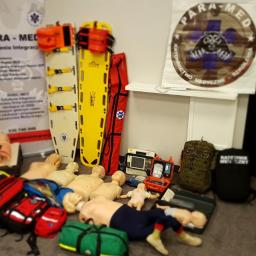 Para-Med Szkolenia Integracja - Fantomy do resuscytacji, deski ortopedyczne, torby medyczne i defibrylator na podłodze, przygotowane do szkolenia z zakresu ratownictwa medycznego.