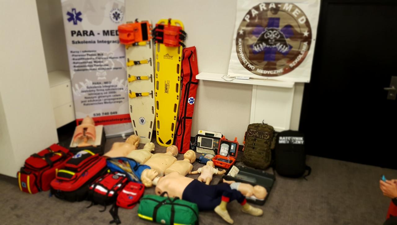 Fantomy do resuscytacji, deski ortopedyczne, torby medyczne i defibrylator na podłodze, przygotowane do szkolenia z zakresu ratownictwa medycznego.