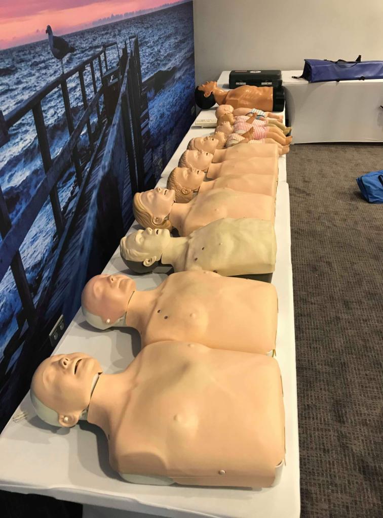 Rząd manekinów do ćwiczeń resuscytacji ułożonych na stole, w tle fototapeta z motywem morskim.