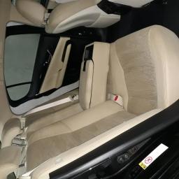 LustrCars - Beżowa, tekstylna tapicerka tylnych siedzeń w samochodzie po czyszczeniu, widoczne pasy bezpieczeństwa i czarne elementy wykończenia wnętrza.