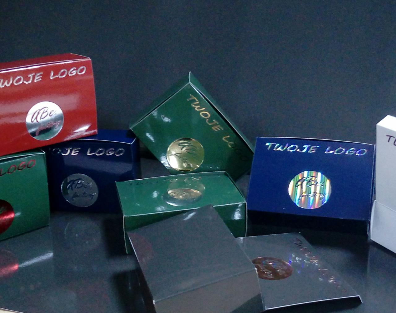 Kolekcja kolorowych pudełek z nadrukowanym logo firmy i błyszczącymi naklejkami, prezentacja różnych wariantów personalizacji opakowań.