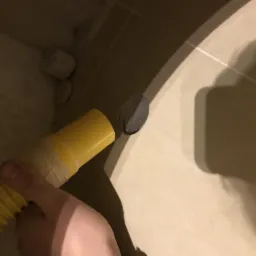 Żółty wąż podłączany do otworu w beżowej płytce ściennej, fragment instalacji w trakcie prac, widoczne pozostałości po wierceniu.