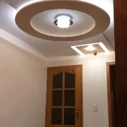 Nowoczesny sufit podwieszany z okrągłym elementem i oświetleniem LED, drewniane drzwi z szybami w tle.