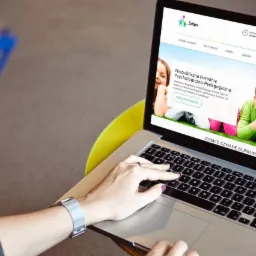 Kobieta z metalowym zegarkiem na ręku pisze na laptopie z wyświetloną stroną internetową poradni psychologiczno-pedagogicznej Salus, z widocznym logo w lewym górnym rogu.