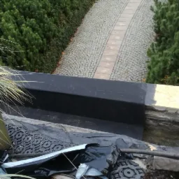 Detale krycia dachu papą termozgrzewalną na balkonie z widoczną kostką brukową i zielenią w tle.