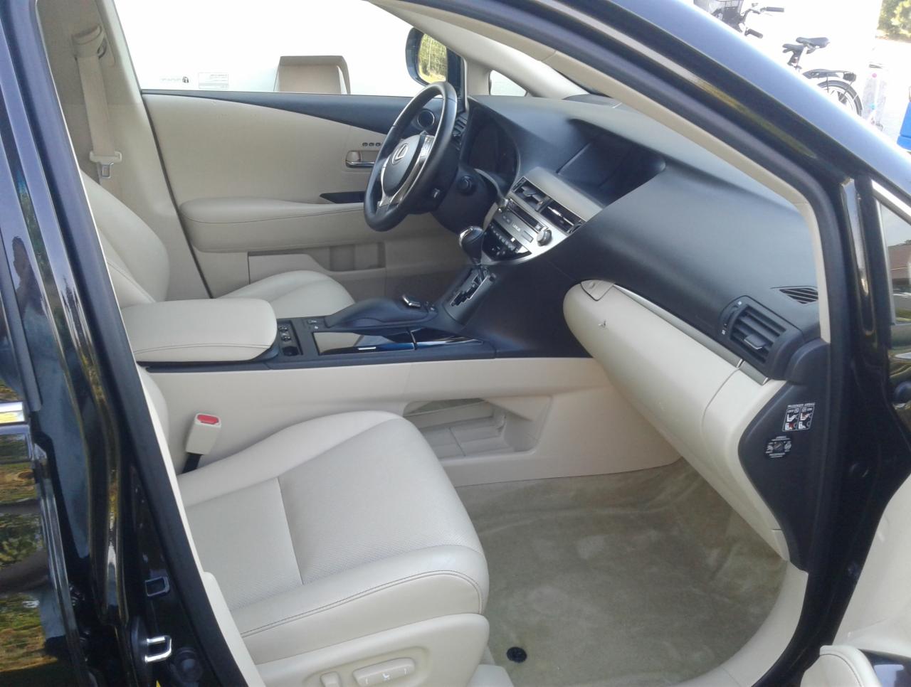 Wnętrze czarnego samochodu marki Lexus z jasną, beżową skórzaną tapicerką, widok z otwartych drzwi na przedni fotel pasażera i deskę rozdzielczą.