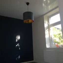 Pomieszczenie po malowaniu ścian na ciemny granat, z widoczną lampą z ażurowym abażurem i złotym wnętrzem, oraz fragmentem zabezpieczonej podłogi.