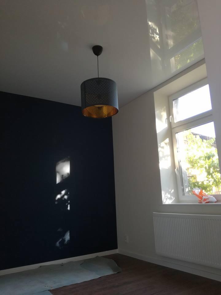 Pomieszczenie po malowaniu ścian na ciemny granat, z widoczną lampą z ażurowym abażurem i złotym wnętrzem, oraz fragmentem zabezpieczonej podłogi.