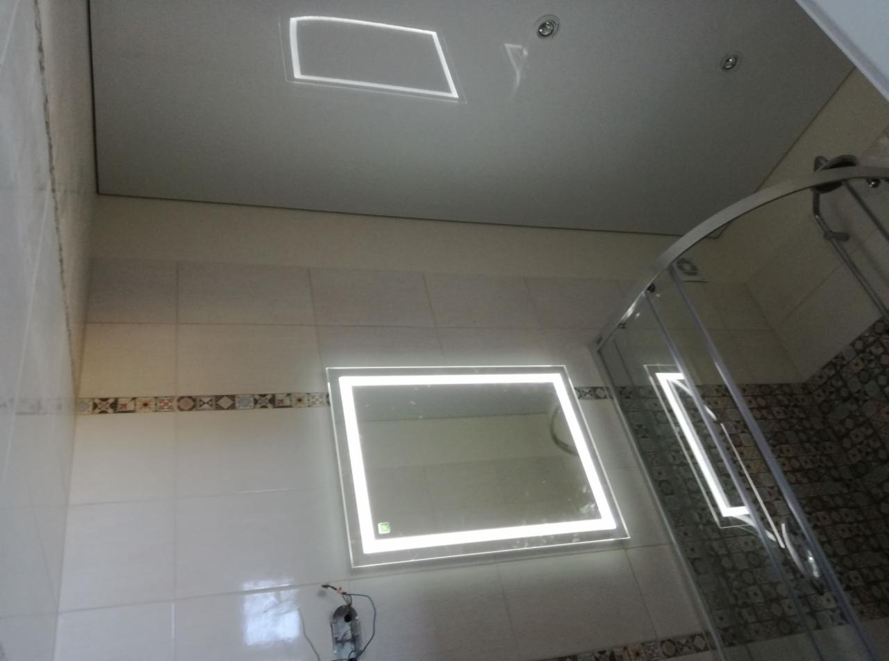 Nowoczesna łazienka z podświetlanym lustrem, kabiną prysznicową z transparentnego szkła i kwadratowym panelem LED w suficie