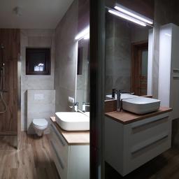 Malgranda - Nowoczesna łazienka z drewnopodobnymi płytkami, kabiną prysznicową typu walk-in, białą umywalką nablatową na szafce z drewnianym blatem oraz lustrem z oświetleniem LED.