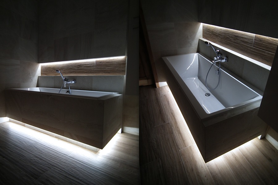 Nowoczesna łazienka z podświetlaną wanną obudowaną panelami imitującymi drewno, oświetlenie LED pod wanną i w półce ściennej, chromowana bateria.