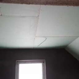 Montaż płyt gipsowo-kartonowych na suficie poddasza, widoczne łączenia płyt i wystający przew&oacute;d elektryczny.