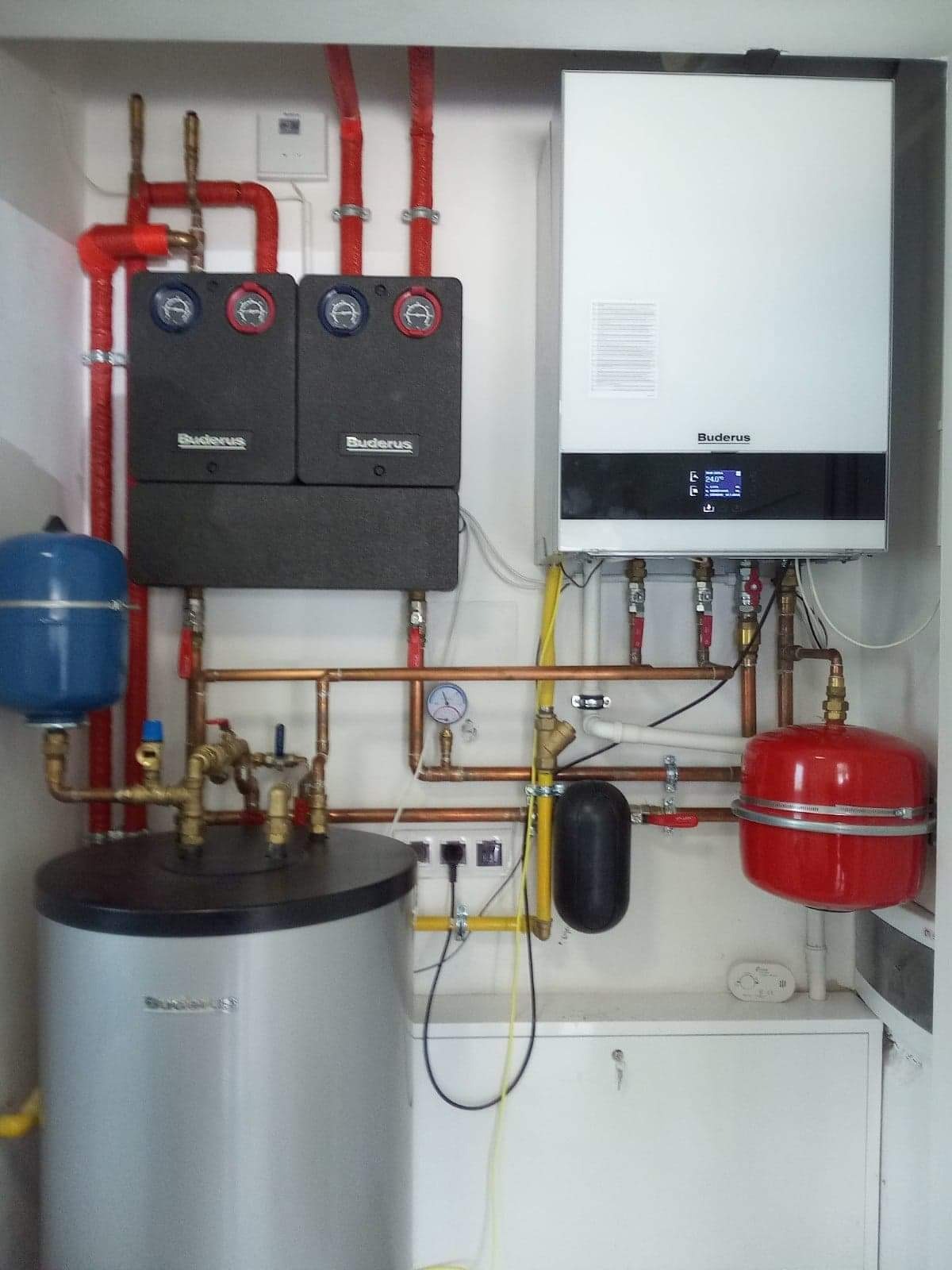 Kompletna instalacja grzewcza Buderus z piecem gazowym, dwoma rozdzielaczami, zasobnikiem ciepłej wody i naczyniami przeponowymi w kotłowni.