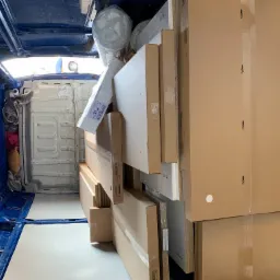 Wnętrze niebieskiego busa wypełnione po brzegi kartonami z meblami i materacem, przygotowanymi do transportu.