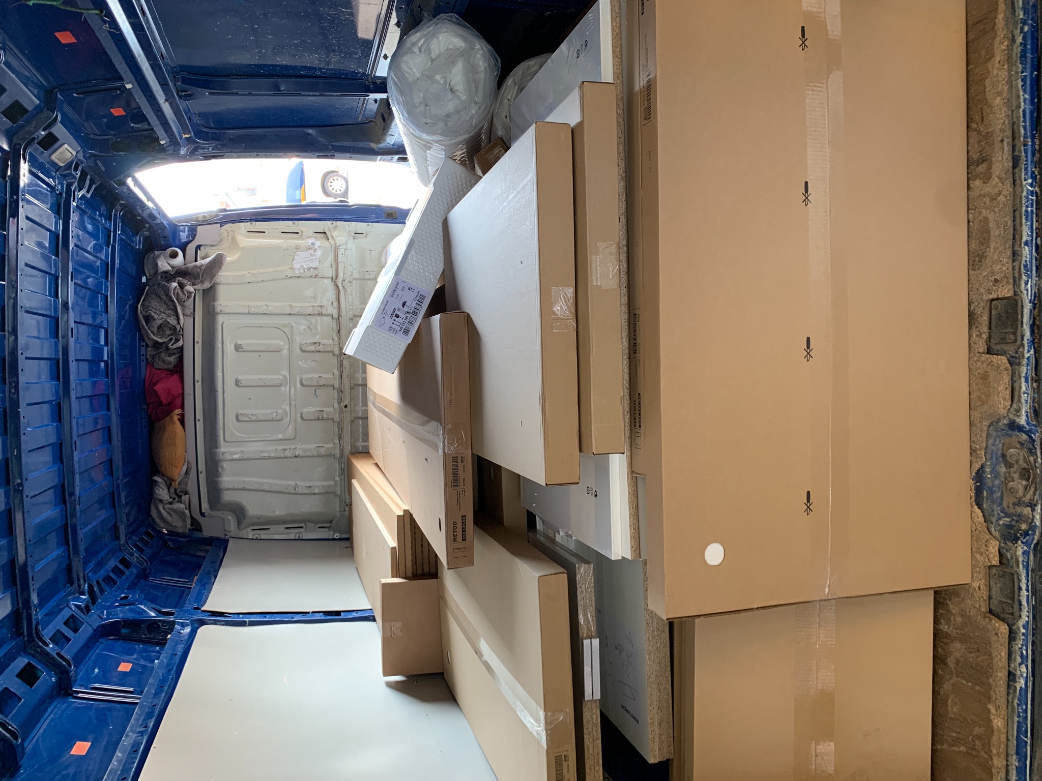 Wnętrze niebieskiego busa wypełnione po brzegi kartonami z meblami i materacem, przygotowanymi do transportu.