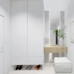 Minimalistyczny przedpokój w bieli: szafa wnękowa, toaletka z lustrem, pufa i abstrakcyjny obraz. Widoczne buty pod szafą. Jasne, naturalne światło.