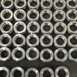 Rząd równo ułożonych, precyzyjnie wykonanych, metalowych pierścieni z wewnętrznym wgłębieniem, leżących na ciemnej powierzchni, z jednym łożyskiem kulkowym w prawym dolnym rogu.