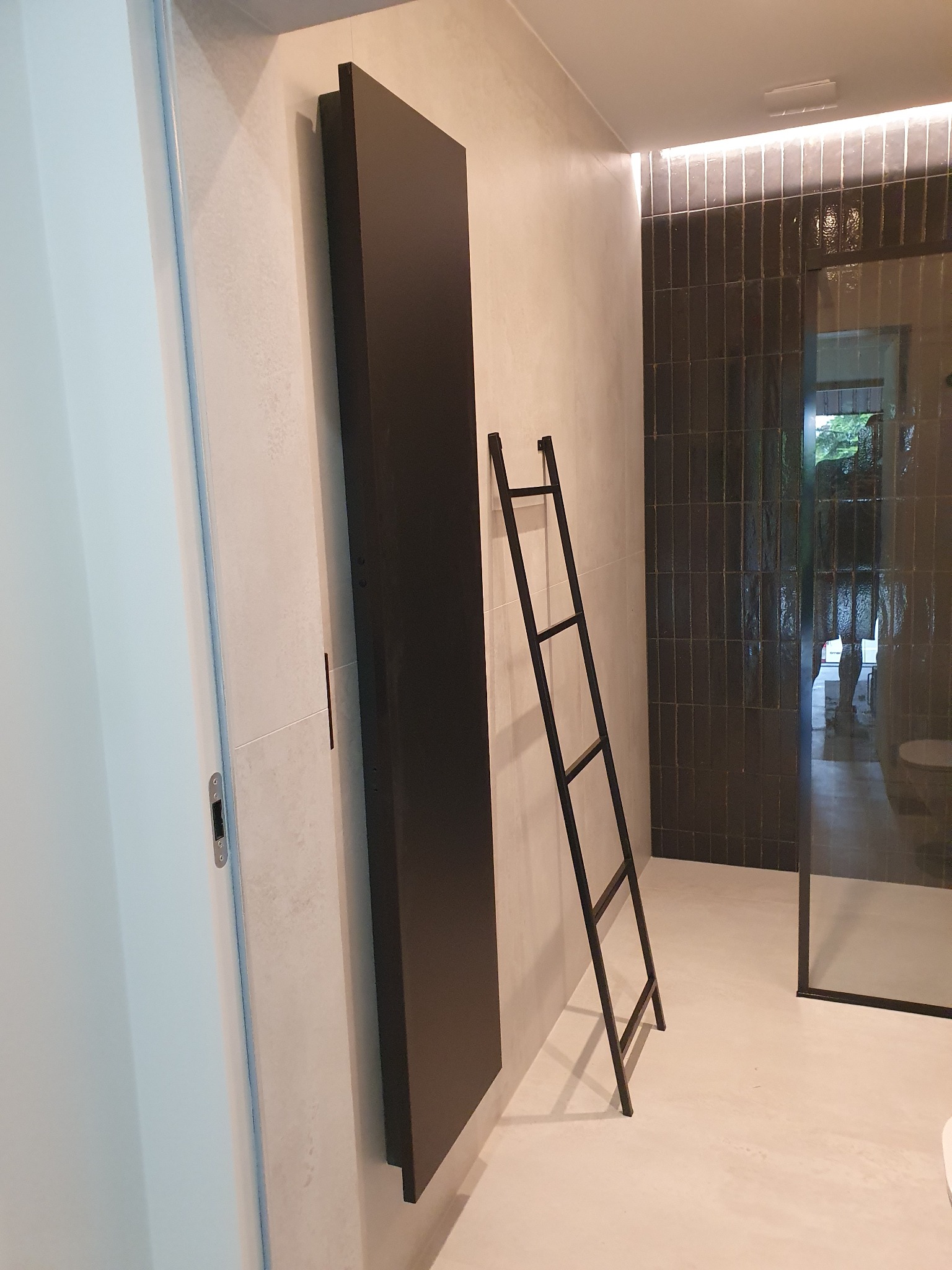Nowoczesna łazienka z czarnym grzejnikiem panelowym, dekoracyjną metalową drabinką i kabiną prysznicową z czarnymi płytkami ułożonymi pionowo.