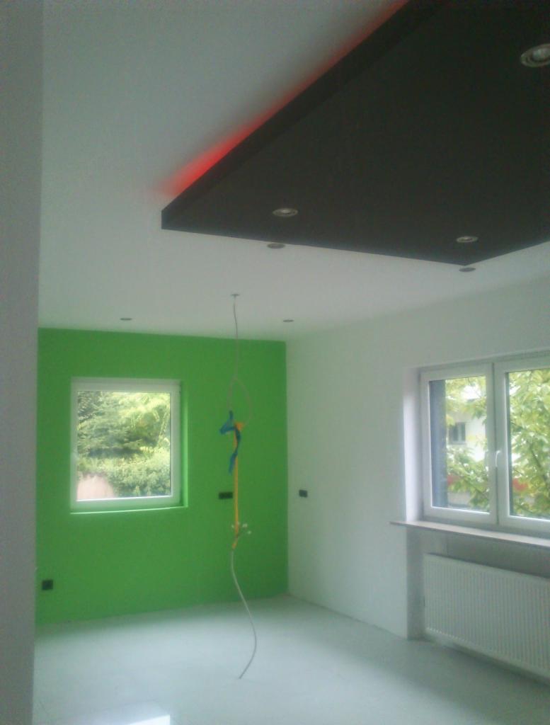 Wnętrze pokoju z zieloną ścianą, podwieszanym sufitem z oświetleniem LED i wystającymi przewodami elektrycznymi.