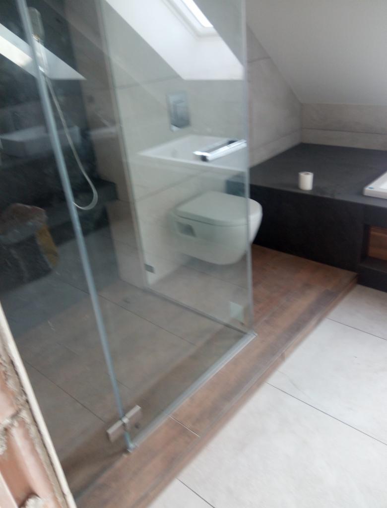 Nowoczesna łazienka na poddaszu z kabiną prysznicową ze szkła hartowanego, wiszącą toaletą i umywalką oraz wykończeniem w odcieniach szarości i brązu.