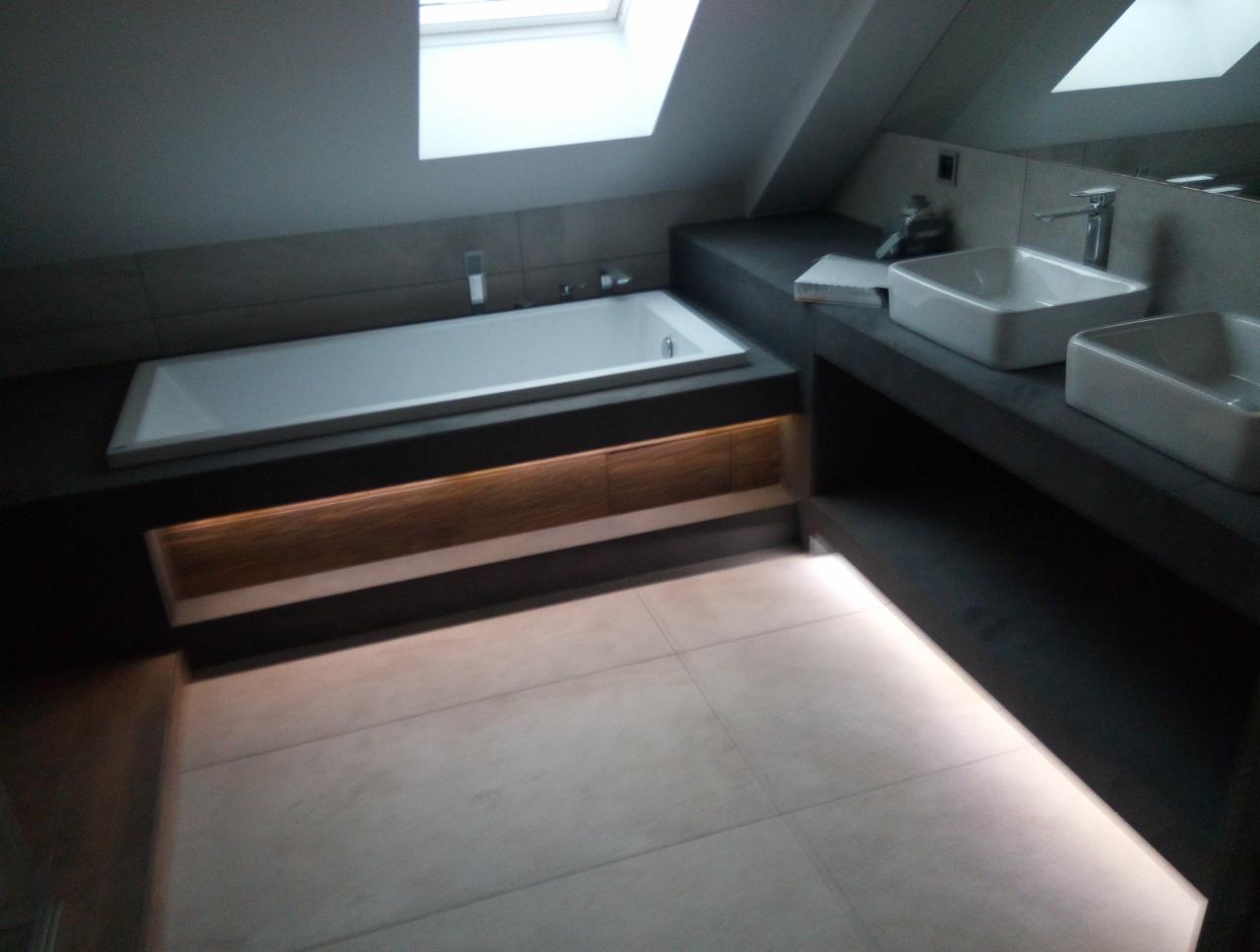 Nowoczesna łazienka na poddaszu z wanną pod oknem dachowym, umywalkami nablatowymi i oświetleniem LED pod wanną oraz szafką.