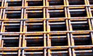 Siatka z prętów zbrojeniowych żebrowanych, widoczne ślady rdzy, ułożona w regularną kratę, oświetlona z góry, ukazana z bliska.