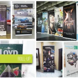 Kolekcja roll-upów reklamowych z różnymi grafikami: koncert, samochody Opel, kosmetyki Amway, herbata Loyd i inicjatywy klimatyczne, ustawione w różnych pomieszczeniach.