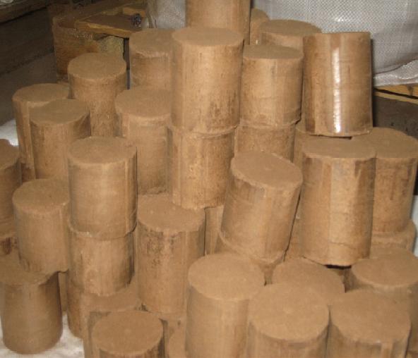 Stos brązowych brykietów paliwowych ułożonych jeden na drugim, widoczne ślady kurzu i drobne pęknięcia na niektórych z nich.