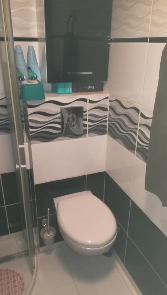 Toaleta podwieszana w łazience wykończonej płytkami z motywem fal, widoczna armatura i akcesoria łazienkowe.