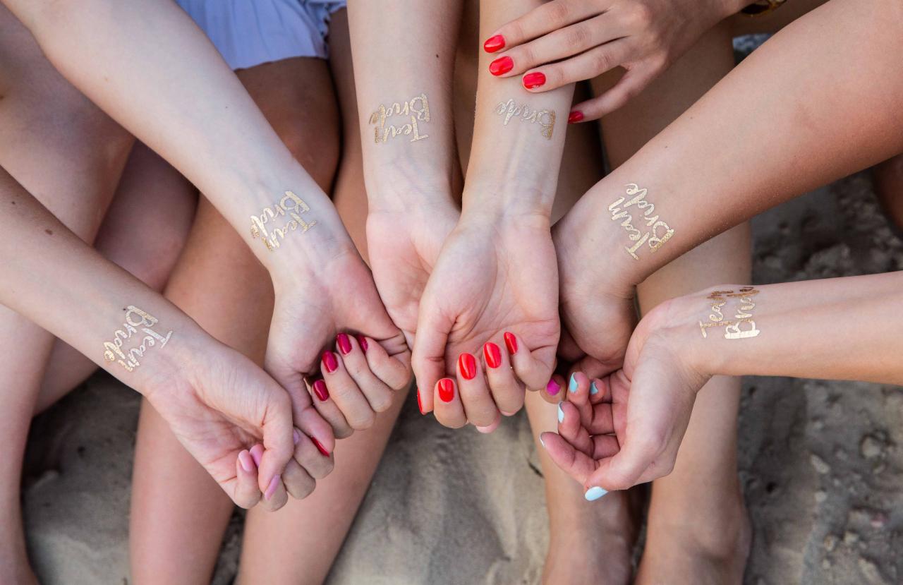 Dłonie kilku kobiet z tymczasowymi tatuażami 'Team Bride', widoczne kolorowe paznokcie, ujęcie z góry.