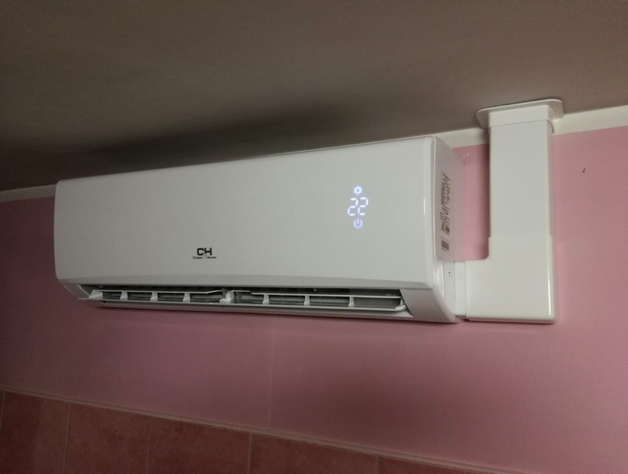 Biały klimatyzator marki CH zamontowany na różowej ścianie, z wyświetlaczem pokazującym temperaturę 22 stopnie Celsjusza.