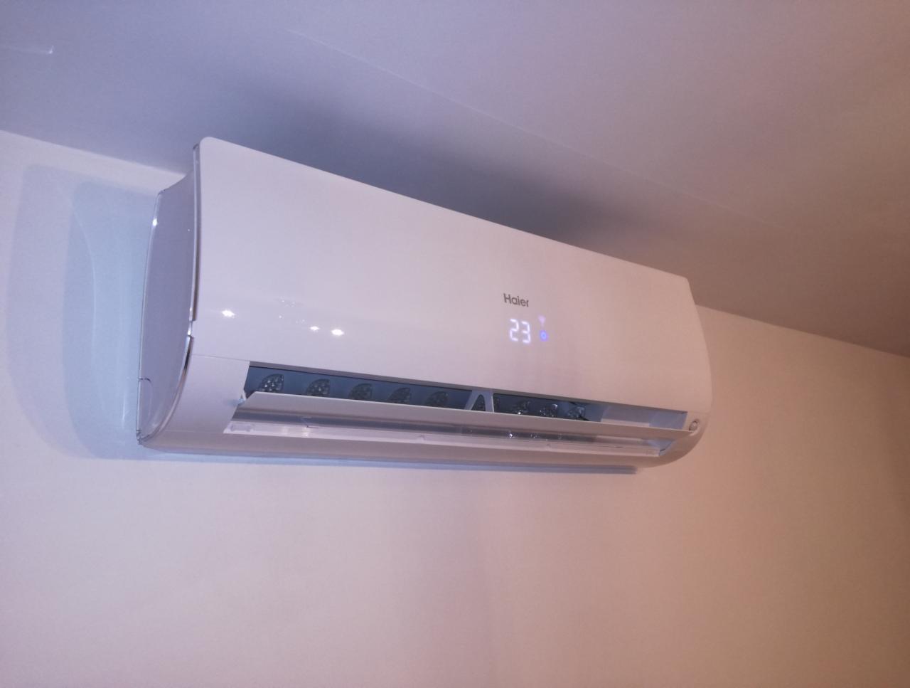 Biały klimatyzator Haier zamontowany na jasnej ścianie, wyświetlający temperaturę 23 stopnie.